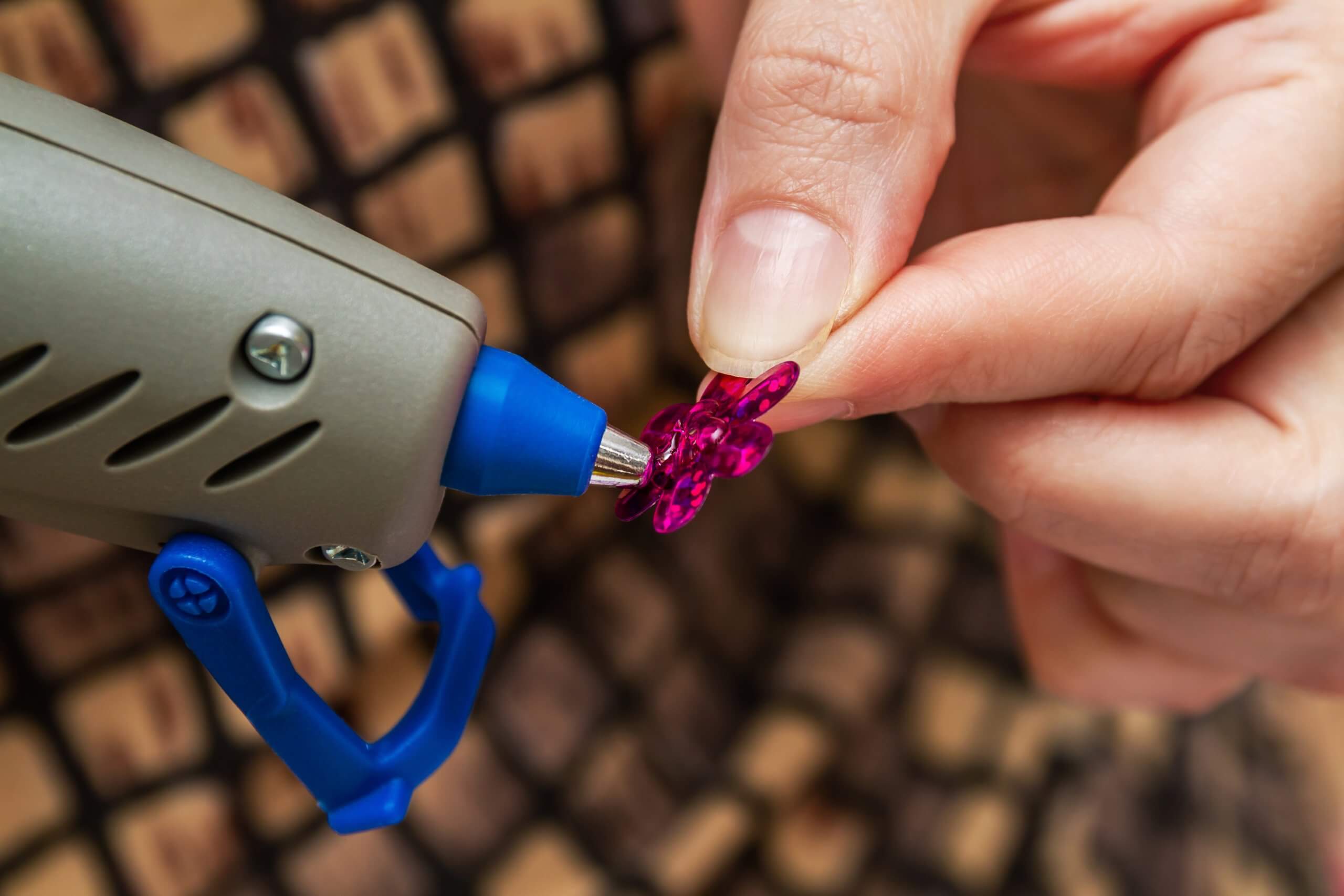 Woman uses hot melt glue gun in handmade applications. Needlewoman glues sequins. Closeup, selective focus